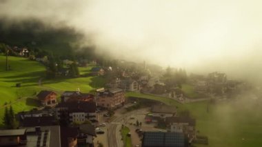 Small town with vintage buildings in summer Alps covered with dense fog. Scenic nature in highland at bright morning sunrise aerial view