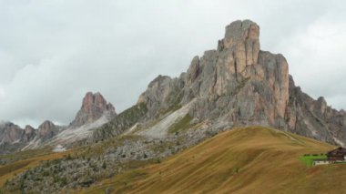 High bare rocky cliff near Giau pass surrounded by meadows for mountain pasture in Dolomites. Small farm situated on gentle slope at breaking sunlight