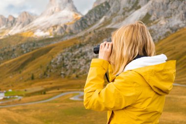 Woman traveling exploring the mountains views covered by clouds looking through binoculars. Travel or travel agency advertising concept. 