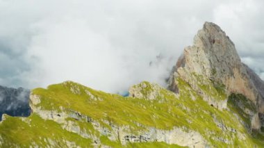 Dense fog surrounds giant Seceda ridgeline with steep grassy slopes on sunny day. Observation point overlooking rocky mountain aerial view