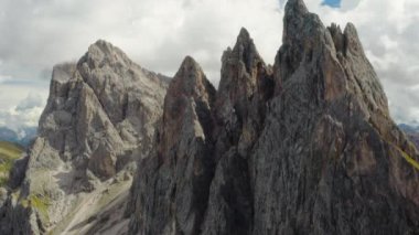 Rocky shady peak of Seceda mountain range against cloudy sky. Summit of long ridgeline in touristic Italian Alps on summer day aerial view