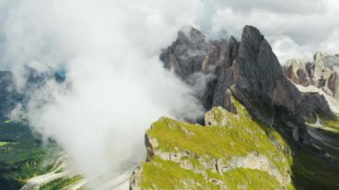 Heavy clouds descended into valley near Seceda mountain with bare peak. Scenic landscape of Italian Alps on sunny summer day aerial view