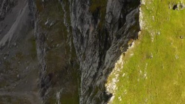 Rocky peak of giant Seceda mountain and slope overgrown with green grass on sunny day. Scenic landscape of Italian Alps under cloudy sky aerial view
