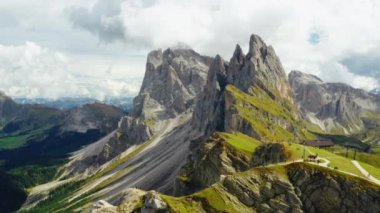 Observation point facing giant rocky Seceda ridgeline under white heavy clouds. Popular tourist destination in Italian Alps aerial view