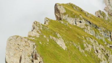 Steep slopes overgrown with green grass in Italian Alps surrounded by dense fog. Giant Seceda mountain range with rocky peak aerial view