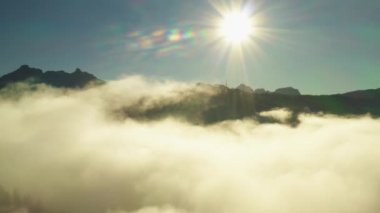 Sun shines bright on clear blue sky illuminating rocky mountain peak of giant Alps. Scenic sunrise and dense fog in highland aerial view