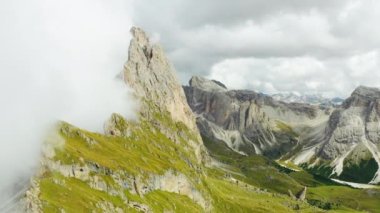 Tourist observation point facing Seceda mountain and dense fog covering bare peak. Rocky ridgeline with steep grassy slopes in Alps aerial view