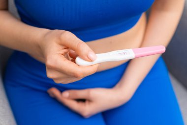 Woman in blue holding a positive pregnancy test and holding the belly. 