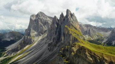 Tourist observation point against Seceda mountain with rocky peaks and green grass under cloudy sky. Scenic Italian Alps in summer aerial view