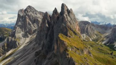 Seceda mountain with bare peak seen from tourist observation point. Giant ridgeline covered with green grass on slopes under cloudy sky aerial view