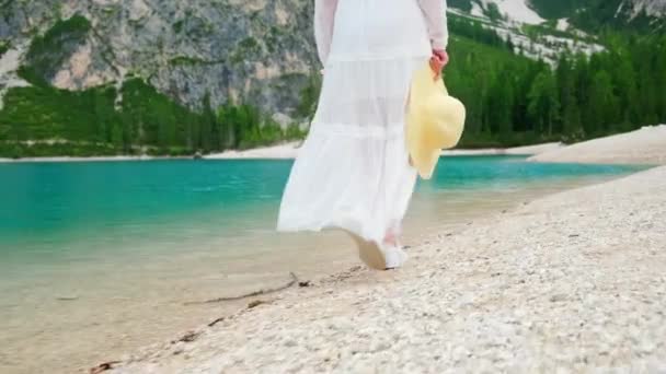 在意大利 一个身穿白衣 手里拿着稻草的女人走在一个绿松石碧水的湖边 摄像机跟着她 — 图库视频影像