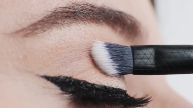 Woman applies bright glitter eyeshadows on eyelid using soft cosmetic brush. Eye makeup process on white background extreme closeup