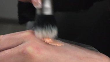 Woman mixes foundation to tone using cosmetic brush and thin film on hand. Beautician prepares beige mixture to apply on face extreme closeup