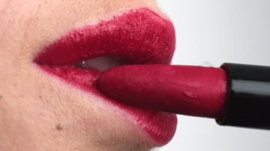 Young woman paints lips in bright red color on white background. Female person applies vibrant lipstick preparing for date extreme closeup