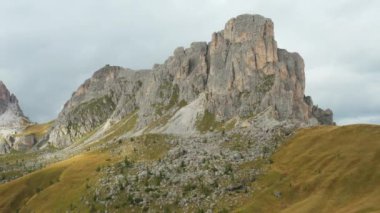 Dolomitler 'de bulutlu gökyüzünün altında, Dolomitler' in otlaklarıyla çevrili, Giau geçidi yakınlarında çıplak kayalıkları olan yüksek bir dağ sırası. Kahverengi otlarla kaplı yumuşak yamaçlar