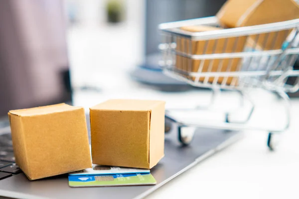 Cardboard boxes and credit card on the laptop and shopping cart on the background.