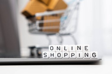 Bilgisayarda duran küplerle ilgili online alışveriş sözcükleri ve karton kutularla dolu bir oyuncak alışveriş arabası arka plan görevi görüyor.