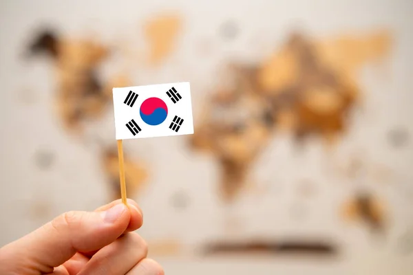 South Korean flag in mans hand on the wooden world map background. Global economy and geopolitics concept.