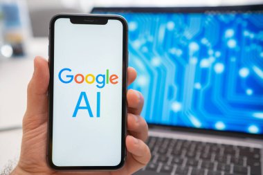 Bir adam tarafından tutulan akıllı telefon ekranında bir Google yapay zeka sinir ağı logosu gösterilirken, arka planda bir dizüstü bilgisayar bir nöronet ile sıçrama ekranı görüntüler. Mart 2023, Prag, Çek Cumhuriyeti 
