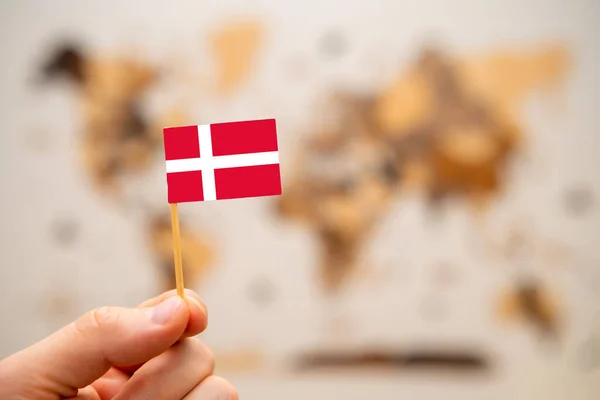 stock image Denmark flag in mans hand on the wooden world map background. Global economy and geopolitics concept. 