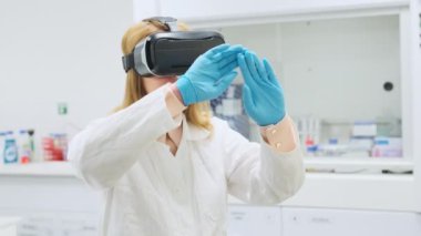 VR gözlüklü bilim adamı doğru olanı seçmek için görüntüyü eliyle kaydırıyor. Genç bir kadın modern laboratuvarda sanal gerçekliği deneyimliyor.