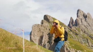İtalyan Alplerinde Seceda Dağı 'nın fotoğraflarını çeken bir adam. Sırt çantalı erkek turist, manzaranın yavaş çekimini yapmak için profesyonel kamera kullanıyor.
