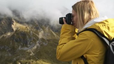Genç bir kadın turist, İtalyan Alplerinde Passo Giau geçidinin güzelliğini profesyonel bir kamerayla yakalıyor. Dağlık bölgede duruyor, yavaş çekimde manzara fotoğrafları çekiyor..
