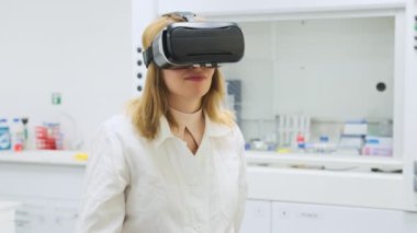 Kadın bilim adamı sanal gerçeklik ayarlarını ayarlamaya çalışıyor. VR gözlüklü genç kadın bilimsel laboratuvarda ağır çekimde el ele hareket ediyor.