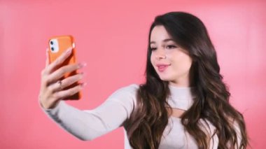 Kahverengi saçlı, neşeli yüzlü bir kadın akıllı telefonuyla sosyal medya için selfie çekmekten hoşlanıyor. Gülümseyen bayan, özçekim fotoğrafları için V hareketi gösteriyor.