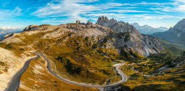 Tre Cime di Lavaredo 'da kayalık dağın eteklerindeki yol rüzgarları. Manzaralı dağ sıraları mavi gökyüzünün altında beyaz bulutlar gün batımında hava manzaralı