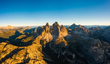 Gün doğumunda Tre Cime di Lavaredo 'nun görkemli silueti. Uçsuz bucaksız dağ manzarası. Kayalık tepeler ve karla kaplı yamaçlar. Arkada aydınlık hava manzarası.