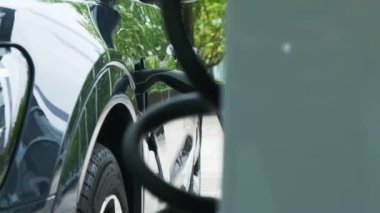 Şehirdeki araç şarj noktasında koyu renk elektrikli araba şarj etme işlemi. Yeşil taşıma konsepti. Elektrik enerjisi mekanik enerjiye dönüştü