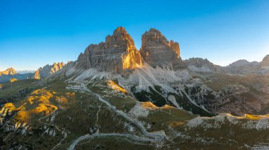 Gün doğumunda yüksek dağların keskin yüzleri. Güneş ışınlarıyla aydınlatılan Tre Cime di Lavaredo 'nun kayalık tepeleri açık gökyüzü manzarası altında aydınlatılıyor.