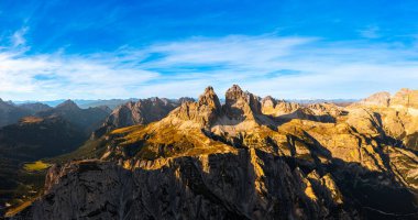 Mavi gökyüzünün altında beyaz bulutlu dağlık Alpler. Rocky tepeleri geniş gölgeli kanyonun üzerinde. Gün batımında Lavaredo 'nun üç tepesi.