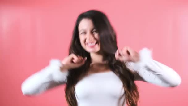 年轻的女人喜欢在粉红的墙壁演播室里带着兴奋而有趣的表情跳舞 黑头发的女士在朋友会上表现出快乐 — 图库视频影像