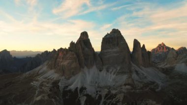 Altın günbatımı renkleri kayalık dağları süslüyor. Tre Cime di Lavaredo eteklerinin siluetli kumla kaplı yamaçları