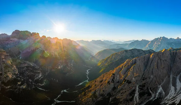 stock image Sharp faces of high mountains at sunrise. Illuminated by sun rays rocky peaks of Tre Cime di Lavaredo under clear sky aerial view in back lit