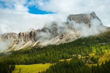 Rocky Dolomite Alpleri 'nin çarpıcı görüntüsü, yüksek zirvenin dağların eteklerindeki ormanla birlikte bulutların arasında kaybolduğu yer..