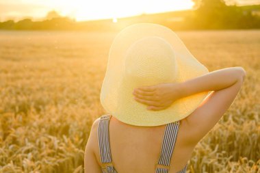 Canlı ayçiçeklerinin arka planında zarif bir bayan duruyor. Hasır şapkası bir nebze cazibe katıyor.