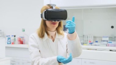 Kadın bilim adamı pipet kullanarak sanal gerçekliği deniyor. VR gözlüklü genç kadın bilimsel laboratuvarda ağır çekimde el ele hareket ediyor.