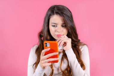 Kadın derin düşünüyor ve cep telefonunu fotokopi alanı olan pembe arka sayfada tutuyor..