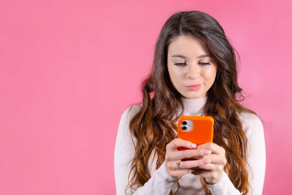 若い女性はピンクの背景にスマートフォンを使用して誰かを不幸にテキストメッセージ — ストック写真