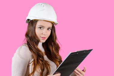 Kasklı genç bir bayan mühendis pembe arka planda projesini elinde tutuyor..