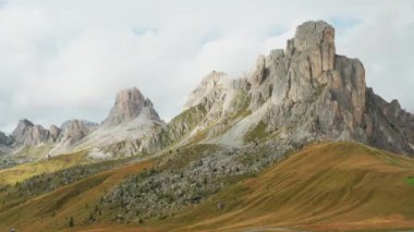 Hiker stands exploring nature of high mountain cliffs around Pass Giau. Female tourist stands on top of hill examining vast mountain valley against blue sky