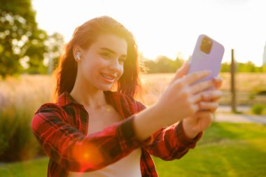 Güzel bir kız, ışıl ışıl bir güneş ışınıyla tarlada fotoğraf çekerek selfie çekiyor.,