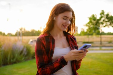 Kulaklıklı genç bir kız, sıradan kırmızı ve siyah bir gömlek giyiyor ve bir arkadaşıyla akıllı telefonunu kullanıyor.. 