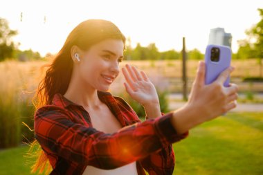 Ekose gömlekli kızıl saçlı bir portre. Genç blogcu, takipçilerine ve kayıt hikayesine cep telefonu kullanarak merhaba diyor.