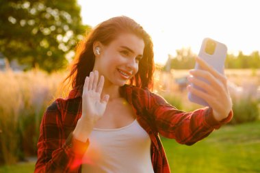 Canlı kızıl saçlı genç bir blog yazarı şık bir ekose gömlek giyip takipçilerini selamlıyor ve akıllı telefon kullanarak günlük hikayesini yakalıyor. 