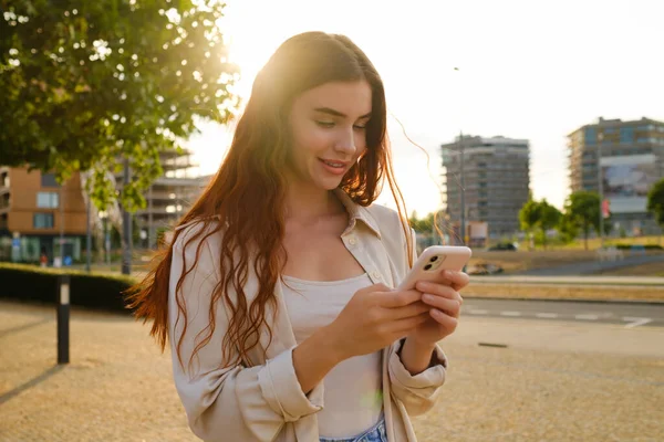 Sokakta dikilen ve gün ışığında cep telefonu kullanan genç bir kadının romantik fotoğrafı..