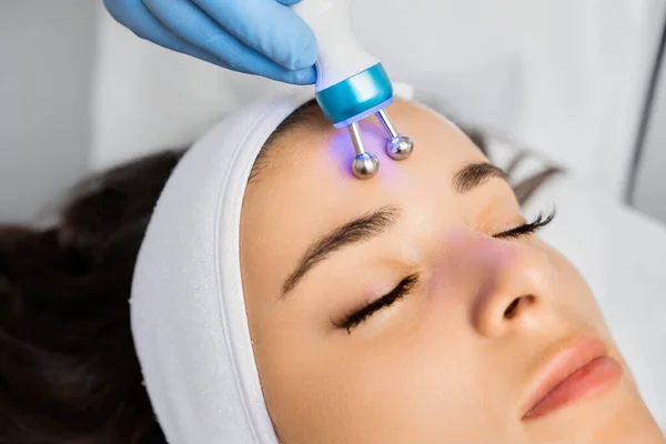 専門家はしわを取り除くために女性の額にマイクロカレントマッサージ装置を使用します — ストック写真